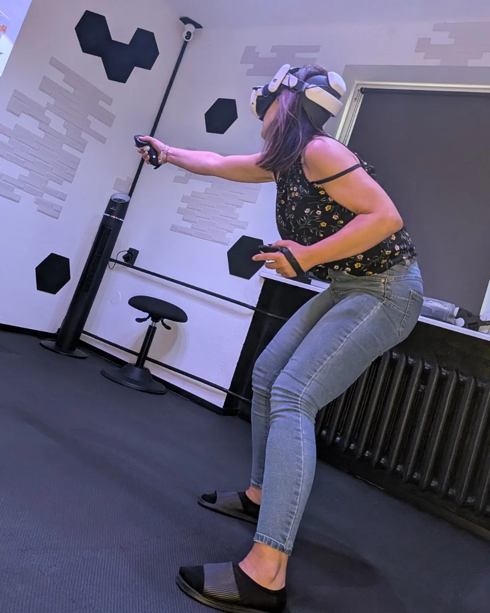 Kobieta w goglach VR trzyma dwa kontrolery i wykonuje dynamiczny ruch w sali WartaRiver.
