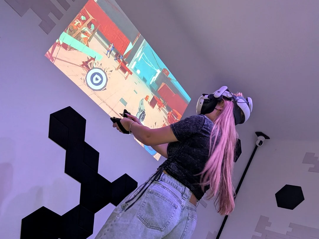 Osoba w goglach VR wyciąga rękę z kontrolerem podczas interakcji.