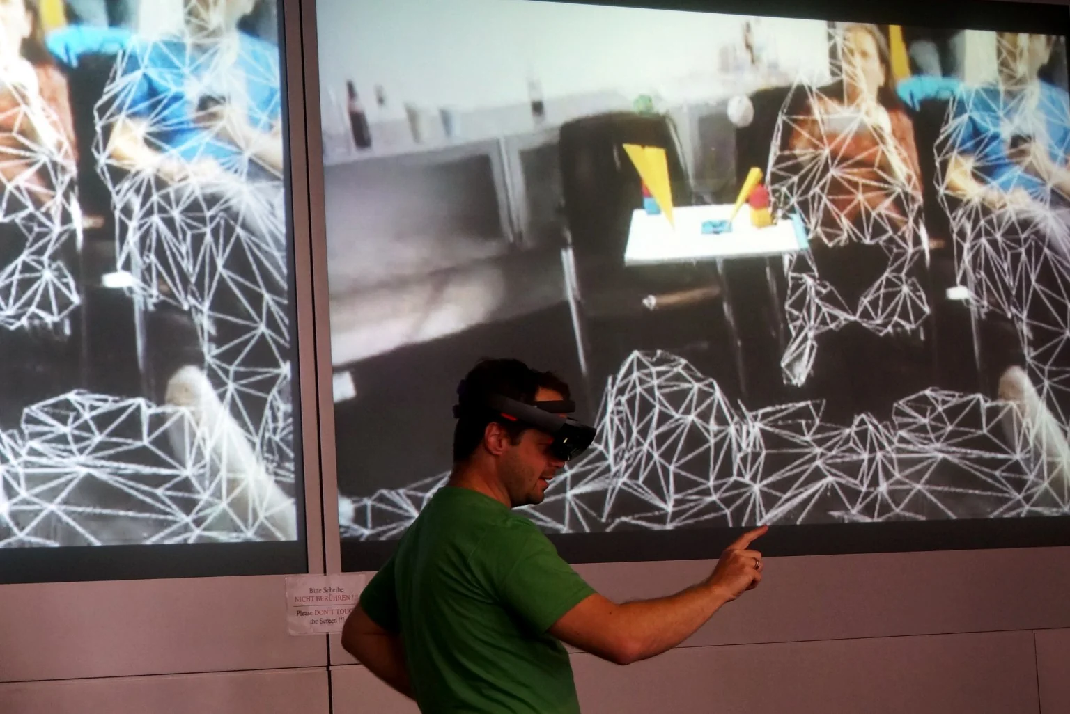 Osoba w zestawie Microsoft HoloLens na tle ekranów pokazujących trójkątną siatkę geometryczną skanowanego pomieszczenia.